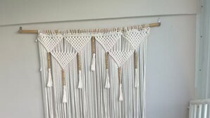 Un pequeño balcón con una mesa redonda, dos sillas de mimbre, un tapiz de macramé y un radiador.