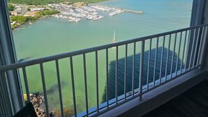 Un balcón con vistas a un puerto deportivo, una colina verde y un cielo despejado.