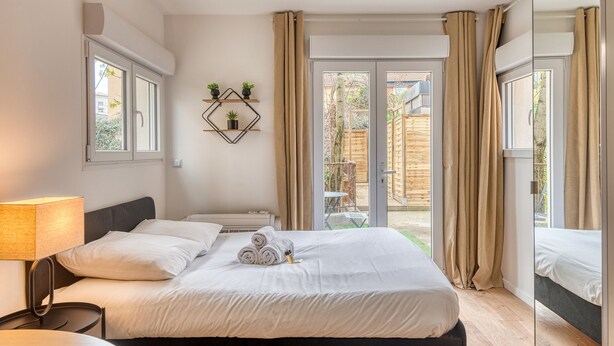 A hotel room with a bed, a bedside table, a lamp, a window, and a view of the outside.