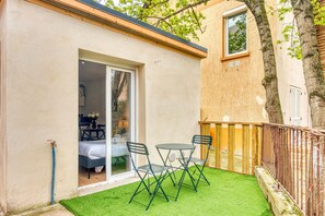 A small patio with a table and chairs, a sliding glass door leading to a bedroom, and a wooden fence.