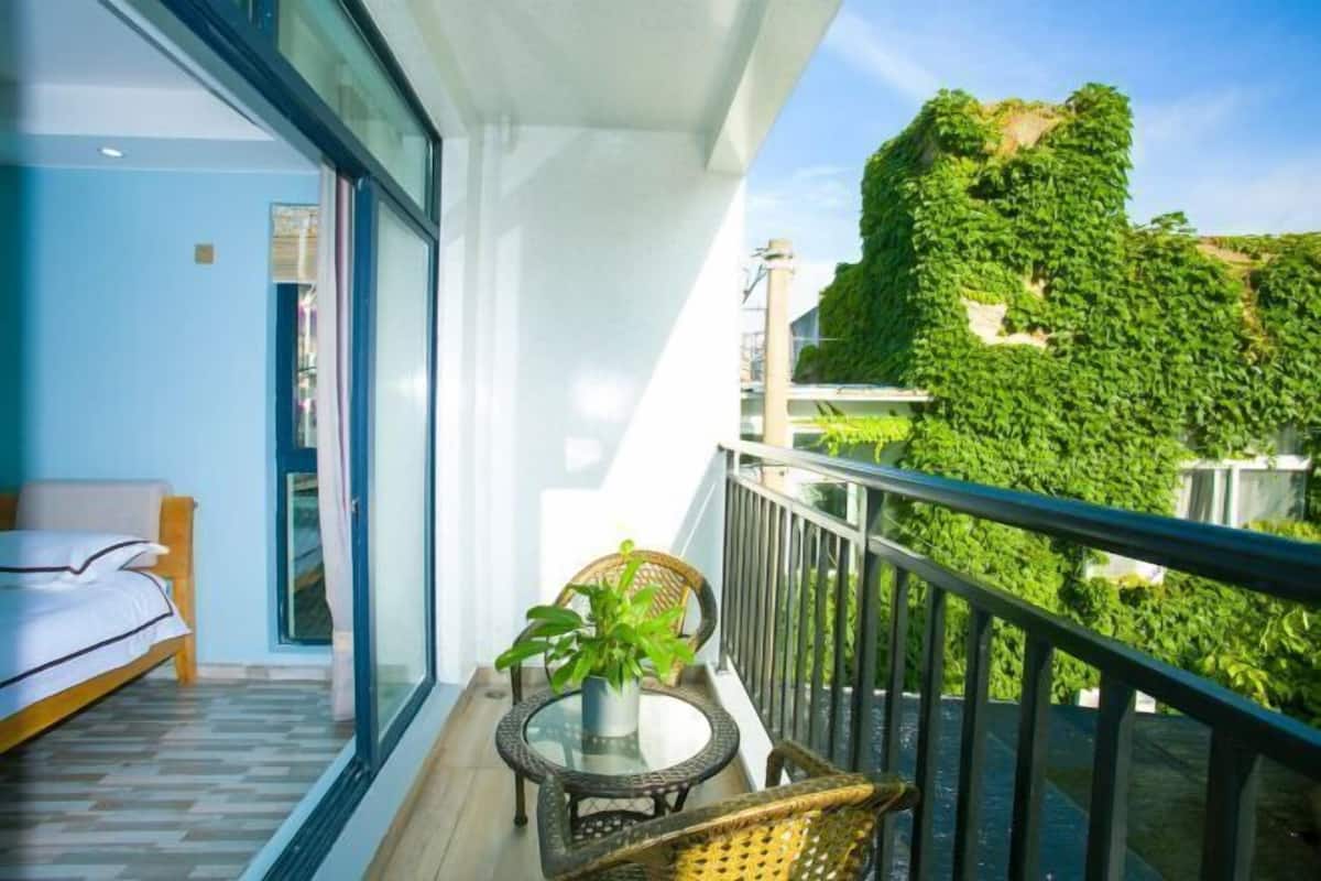Un balcón con una cama, una mesa con una planta y vista a una pared verde.