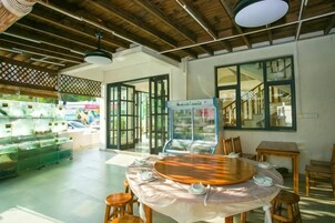 Un restaurante con techo de madera, una mesa redonda con sillas y una vitrina de vidrio con productos alimenticios.