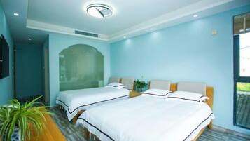 A hotel room with two beds, a wooden desk, a potted plant, and a large window.