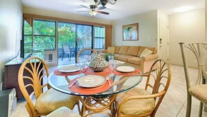 Un coin repas avec une table en verre, des chaises en osier et un ventilateur de plafond.