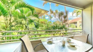 Un balcon avec une table dressée pour deux personnes, donnant sur un jardin luxuriant agrémenté de palmiers et sur lequel on aperçoit un bâtiment au loin.