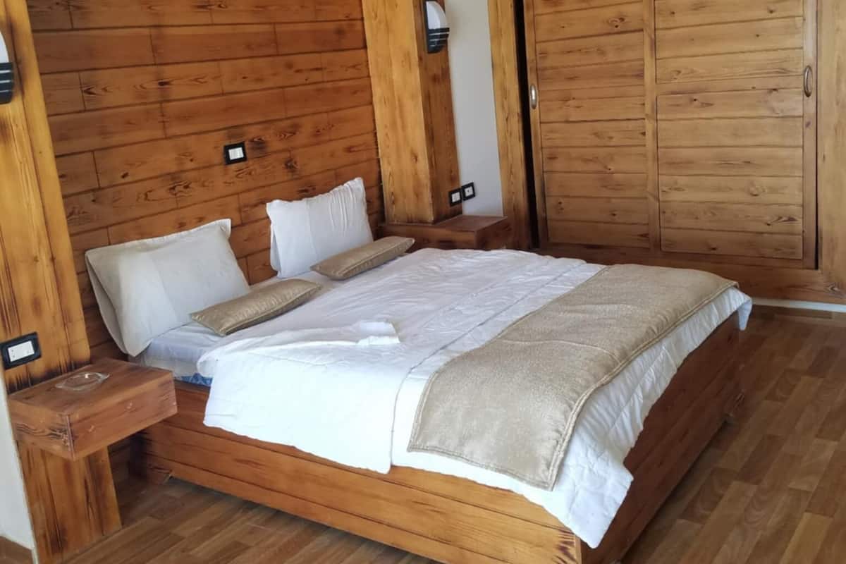 Una cama de madera con ropa blanca, una mesita de noche y un armario de madera.