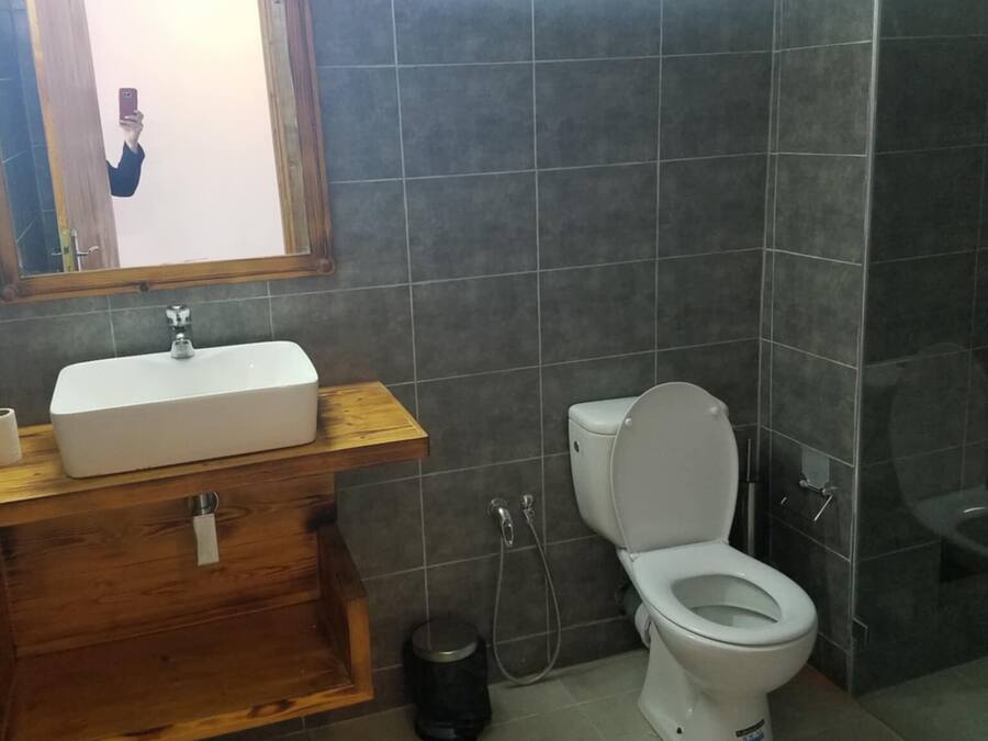 Une salle de bain avec un meuble-lavabo en bois, un lavabo blanc, des toilettes et un espace douche.