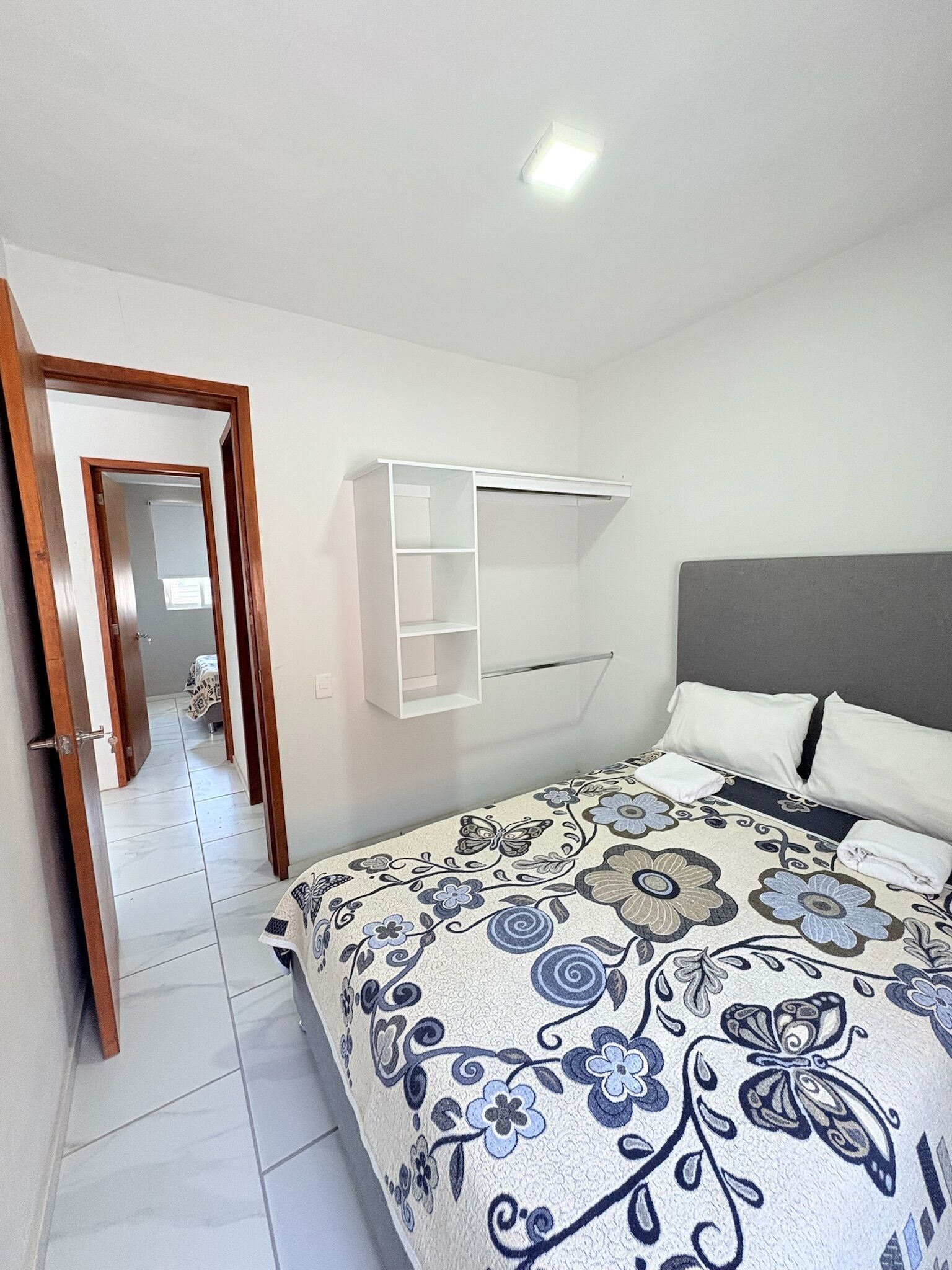 A bedroom with a bed, a white wardrobe, and a door leading to another room.