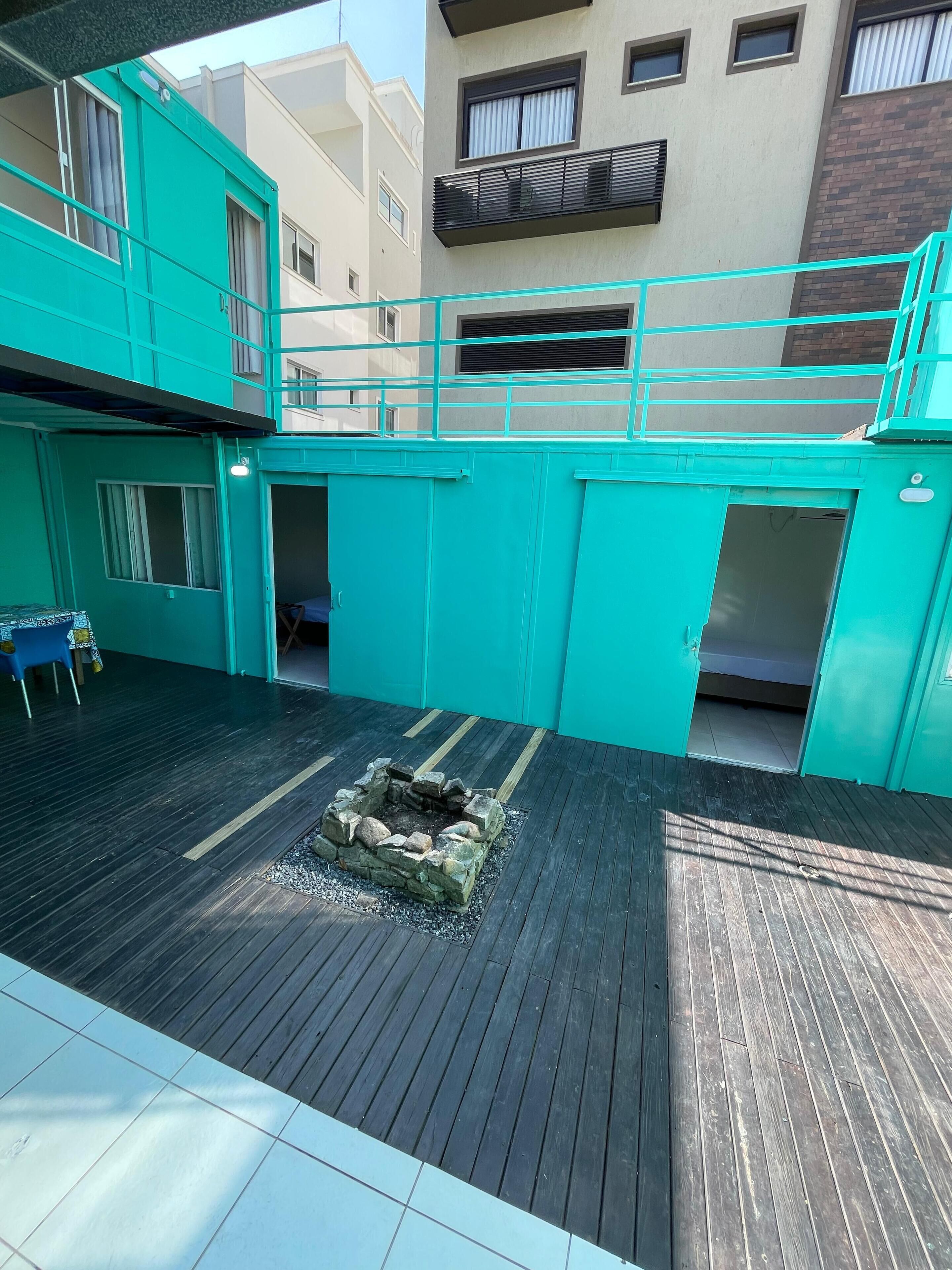 A turquoise-colored building with a wooden deck, a fire pit, and a blue chair.