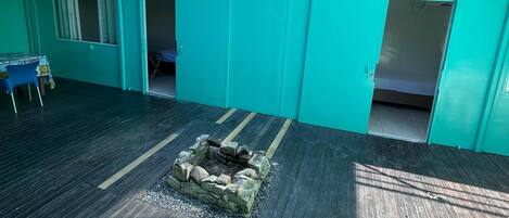 A turquoise-colored building with a wooden deck, a fire pit, and a blue chair.