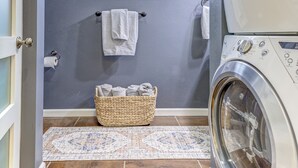 Un cuarto de lavado con lavadora, una ventana, un tendedero y una cesta con toallas dobladas.