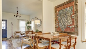 Un comedor con una mesa y sillas de madera, una araña y un mapa en la pared.