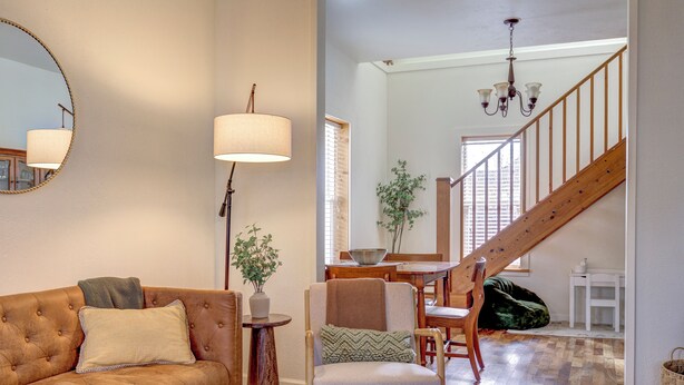 Una sala de estar con un sofá de cuero marrón, una silla de madera, una mesita con un cuenco y una escalera que lleva a otra habitación.