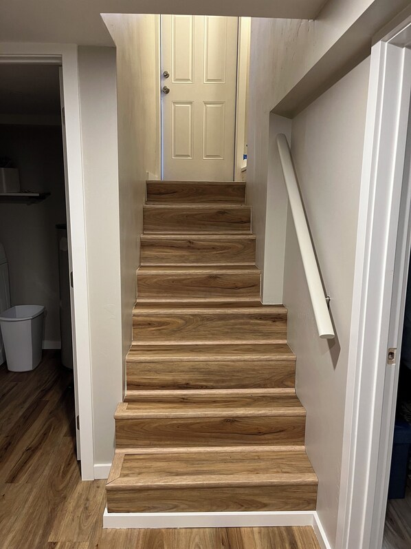 A wooden staircase with a handrail, leading to a white door.