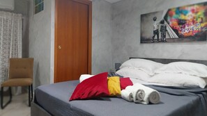 Hotellihuone, jossa on sänky, tuoli, ovi ja taulu seinällä.