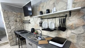 Une cuisine moderne avec un mur en pierre, un téléviseur à écran plat, une machine à café, un évier et un réfrigérateur.