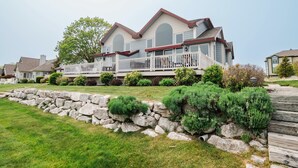 A two-story house with a balcony, stone retaining wall, and well-maintained lawn.