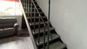 A modern staircase with a metal railing, wooden steps, and a view of a living room with a sofa and a window.