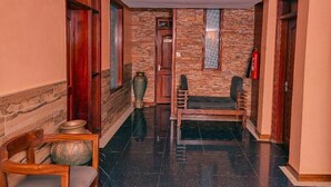 A hallway with a stone wall, a wooden bench, and a fire extinguisher. - Sheron Hotel Kampala (Kampala)