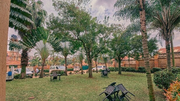 An outdoor area with grass, trees, and outdoor seating. - Sheron Hotel Kampala (Kampala)