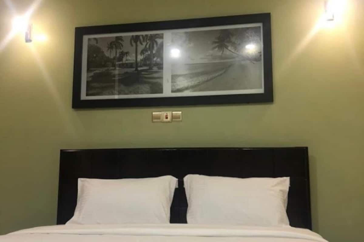 Cama bem arrumada com lençóis brancos em quarto com paredes verdes.