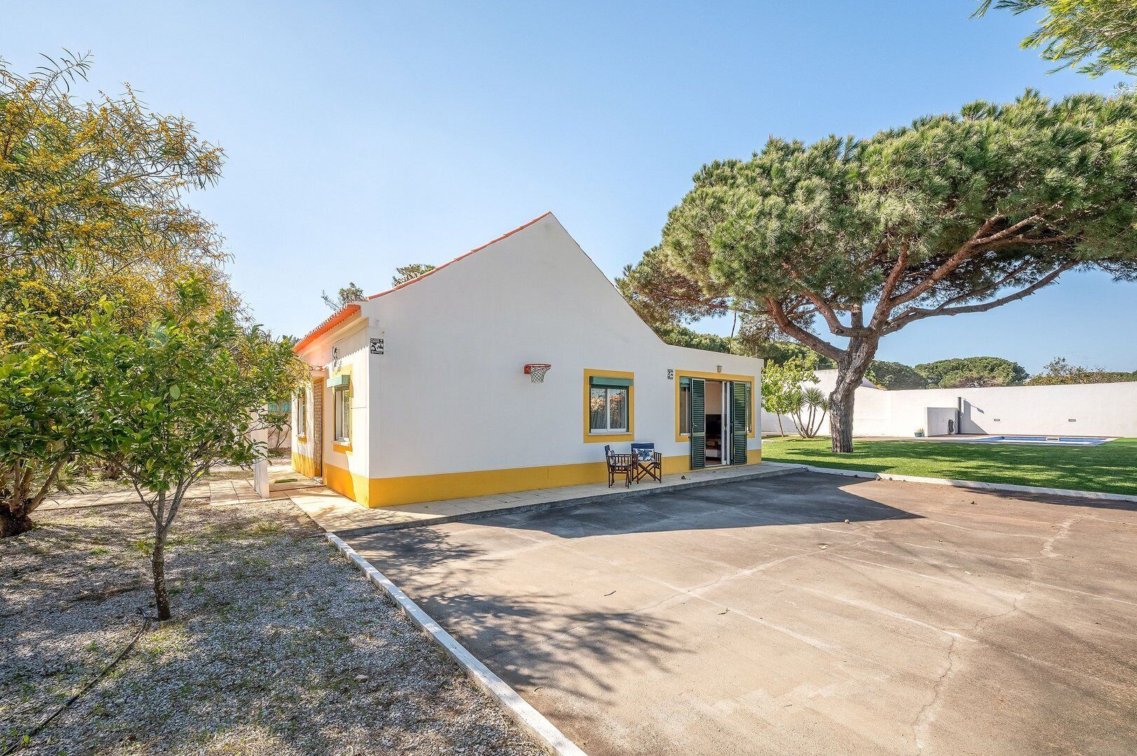 Ein eingeschossiges Gebäude mit geneigtem Dach, einer kleinen Veranda mit Tisch und Stühlen sowie einem Basketballkorb.