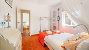 A bedroom with a bed, a dresser, a wardrobe, a wardrobe mirror, a bedside table, a lamp, a window with a view, and a door leading to another room. - GuestReady - Peaceful vacation with pool (Setúbal)