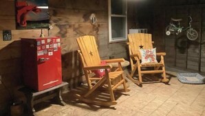 A cozy room with wooden walls, two rocking chairs, a red vending machine, and a window with a bicycle hanging outside. - Luxury in the country! The Dog- lovin’ Rockin' K offers A/C, WiFi and views! (Reed Point)