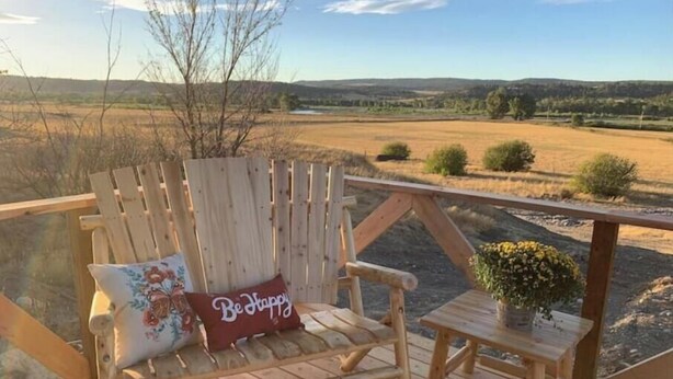 A wooden deck with a wooden chair and a small table, overlooking a scenic landscape. - Luxury in the country! The Dog- lovin’ Rockin' K offers A/C, WiFi and views! (Reed Point)