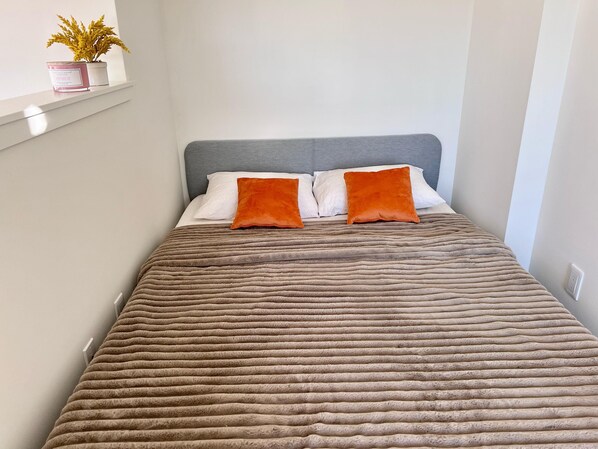 Un lit avec une tête de lit grise, deux oreillers orange et une couverture marron à texture.