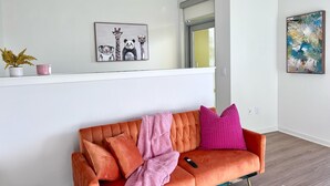Un salon moderne avec un canapé, un tableau représentant des animaux, une plante en pot et une fenêtre.