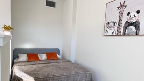 Une chambre à coucher avec un lit, des oreillers, une œuvre d’art accrochée au mur et une petite plante.