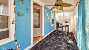 Una habitación con pared azul, ventilador de techo, una mesa con sillas y una ventana con cortinas.