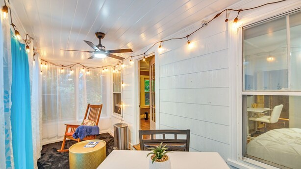 Una habitación acogedora con ventilador de techo blanco, luces colgantes, una mesa de comedor y un ventanal grande.