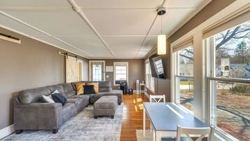 A modern living room with a sectional sofa, a dining table, and large windows offering a view of the outdoors.