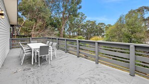Une terrasse extérieure avec une table et des chaises, une balustrade et des arbres en arrière-plan.