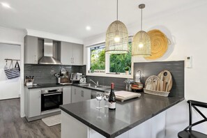 A modern kitchen with a central island, stainless steel appliances, and a view of greenery outside. - Fair Waves (Lorne)