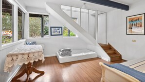 Une pièce avec un escalier, une table recouverte d’une nappe en dentelle et un tableau encadré accroché au mur.