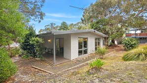 Une petite maison de plain-pied, dotée d’un porche abrité, de grandes fenêtres et offrant une vue sur les arbres environnants.