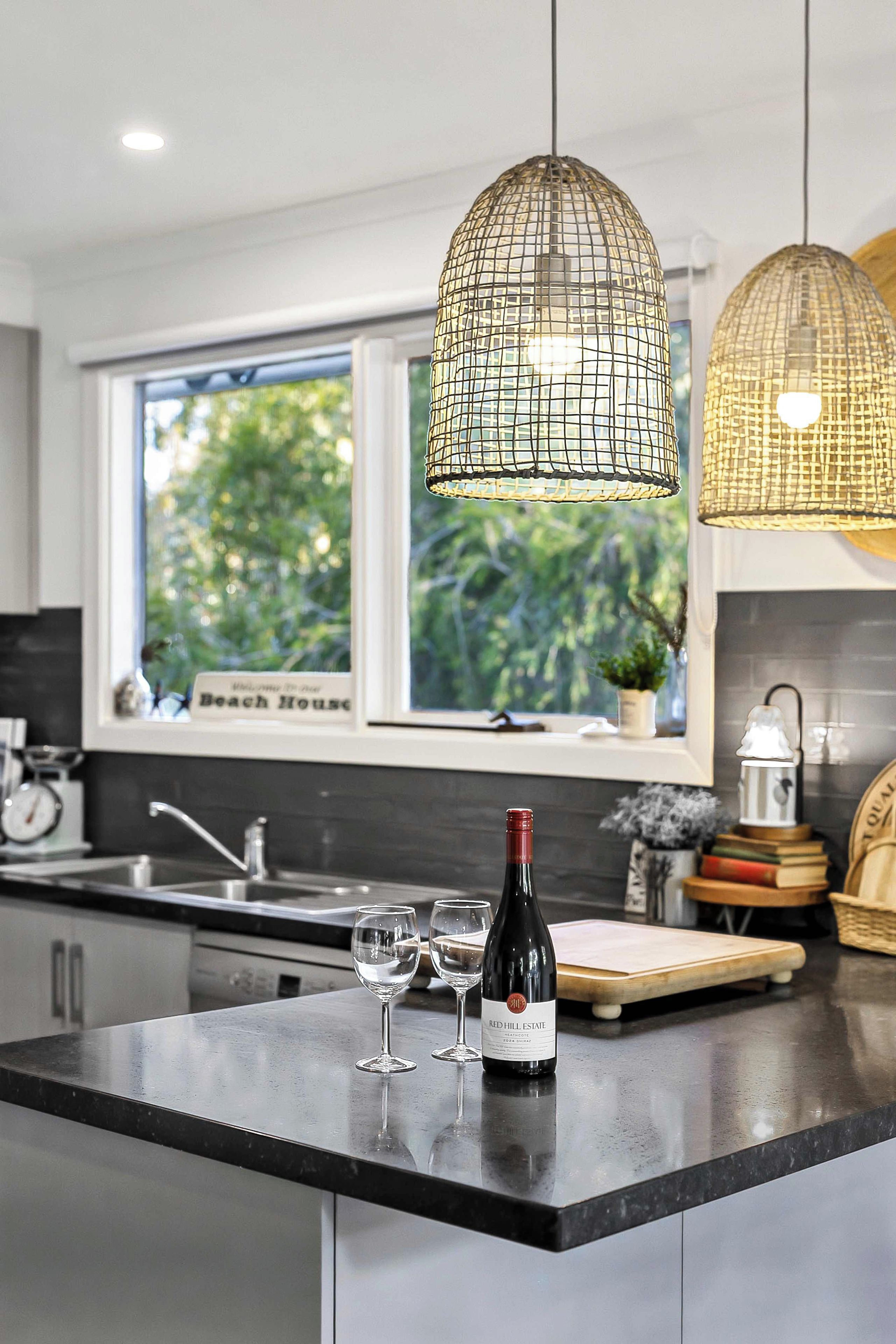 A modern kitchen with a large window, pendant lights, a wine bottle, and glasses on the counter.