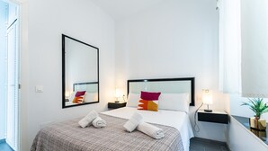Une chambre d’hôtel avec un grand lit, deux tables de chevet, un miroir et une plante en pot.