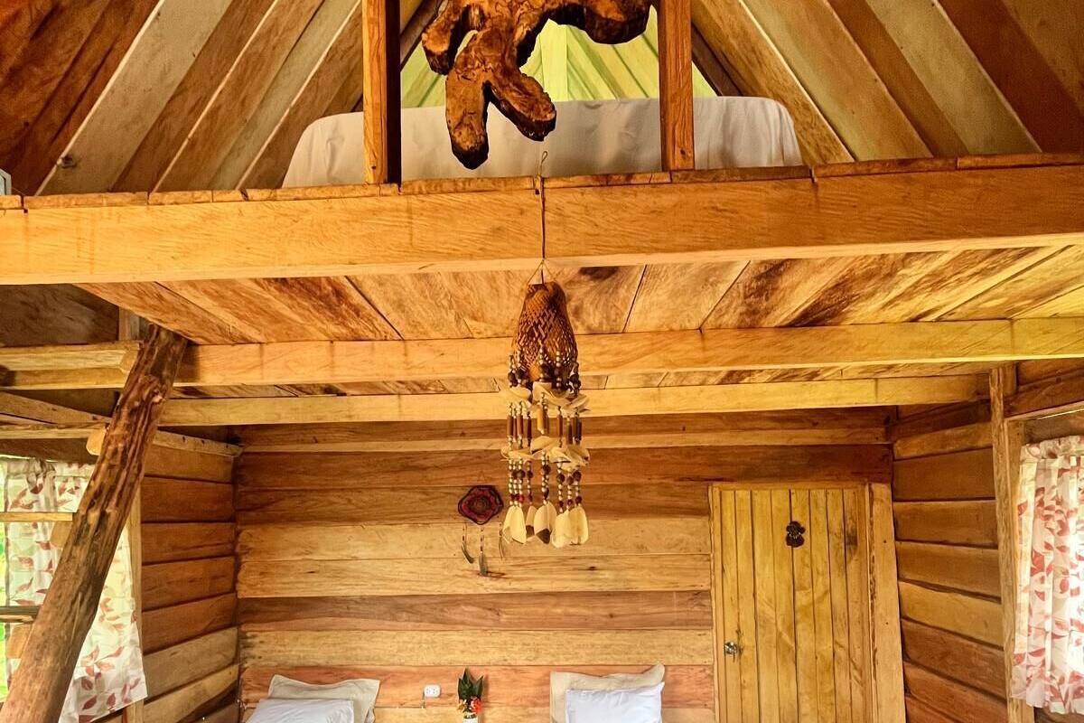 A wooden cabin with two single beds, a wooden ceiling, and a rustic decor including a hanging ornament.