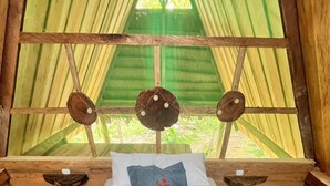 A bed with a blue and white bedspread, two pillows, and a decorative pillow with a red leaf design. There are towels folded on the bed and a small table with a cup and a tissue box. - Pura Chata Ecolodge (San Juan Bautista)