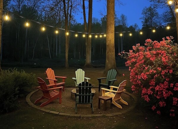A circular seating area with Adirondack chairs and a small table, surrounded by a string of lights and a flowering bush. - Dock To Do Little lakefront w/boat slip & firepit (Scottsboro)