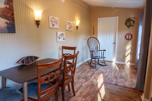 A dining area with a wooden table and chairs, wall-mounted light fixtures, and framed artwork on the wall. - Dock To Do Little lakefront w/boat slip & firepit (Scottsboro)