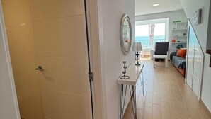 Un intérieur moderne avec un plancher en bois, une porte blanche, une petite table avec une lampe et une vue sur l’extérieur.