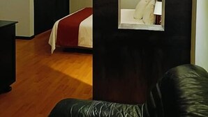 A hotel room with a bed, a black leather sofa, a mirror, and a wooden floor. - Hotel & Suites Virreynal (Teziutlán)