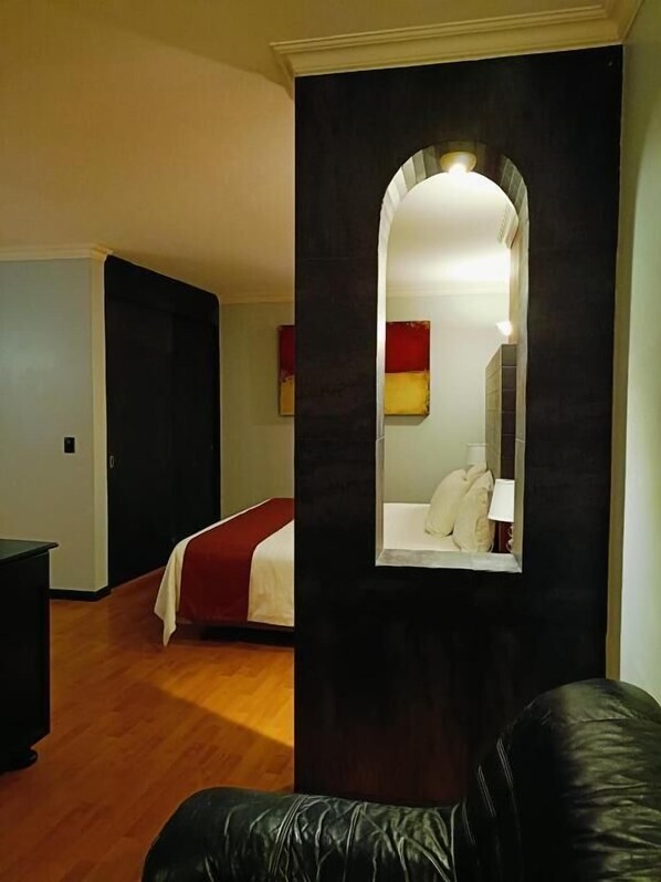 A hotel room with a bed, a black leather sofa, a mirror, and a wooden floor.