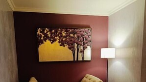 A living room with a beige sofa, two ottomans, a floor lamp, and a painting of trees on the wall. - Hotel & Suites Virreynal (Teziutlán)