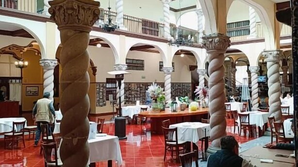 A spacious indoor area with high ceilings, multiple levels, and a central open space surrounded by tables and chairs. - Hotel & Suites Virreynal (Teziutlán)